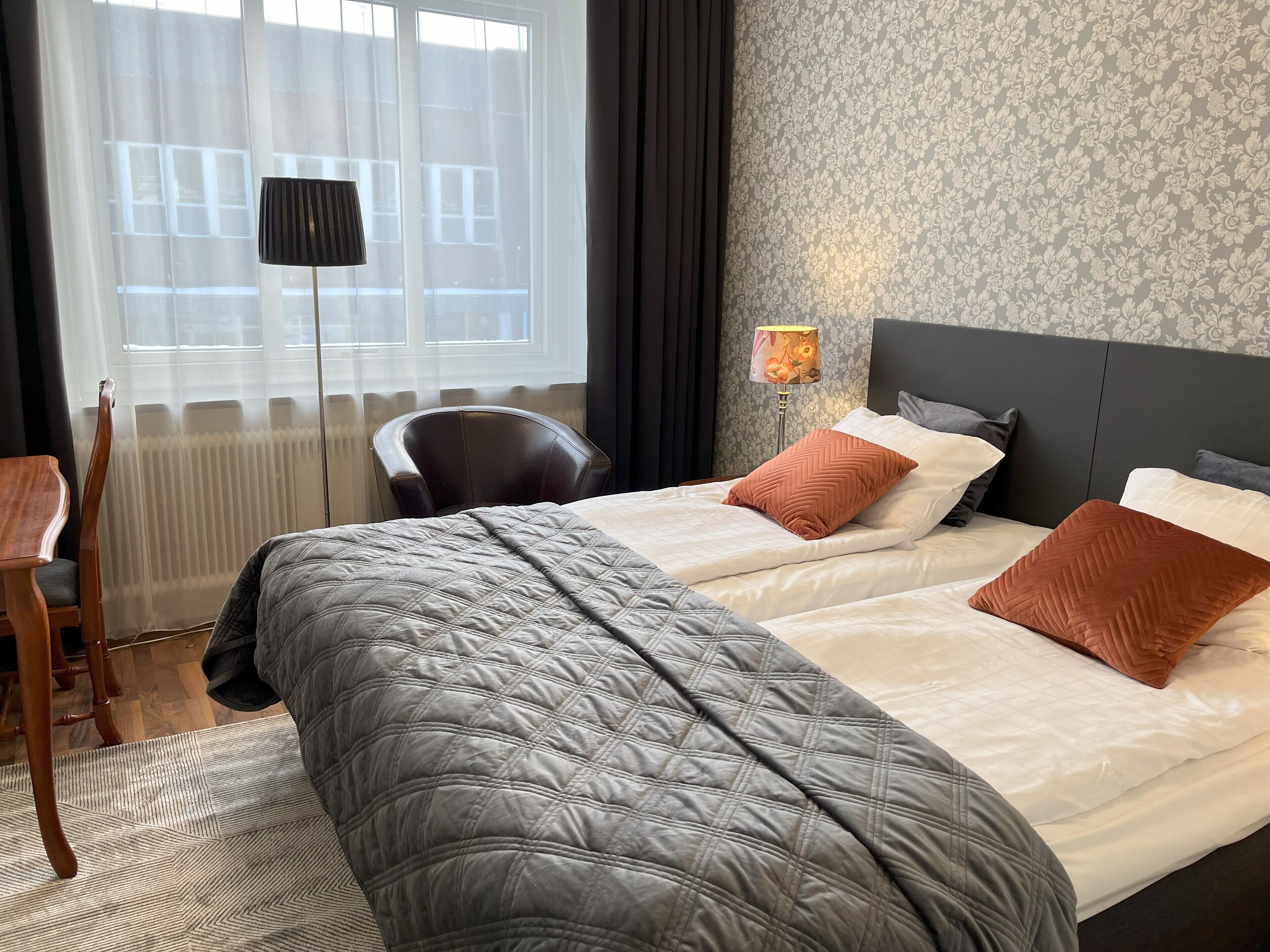 A hotel room with two beds, a chair, a desk, and a window with curtains.