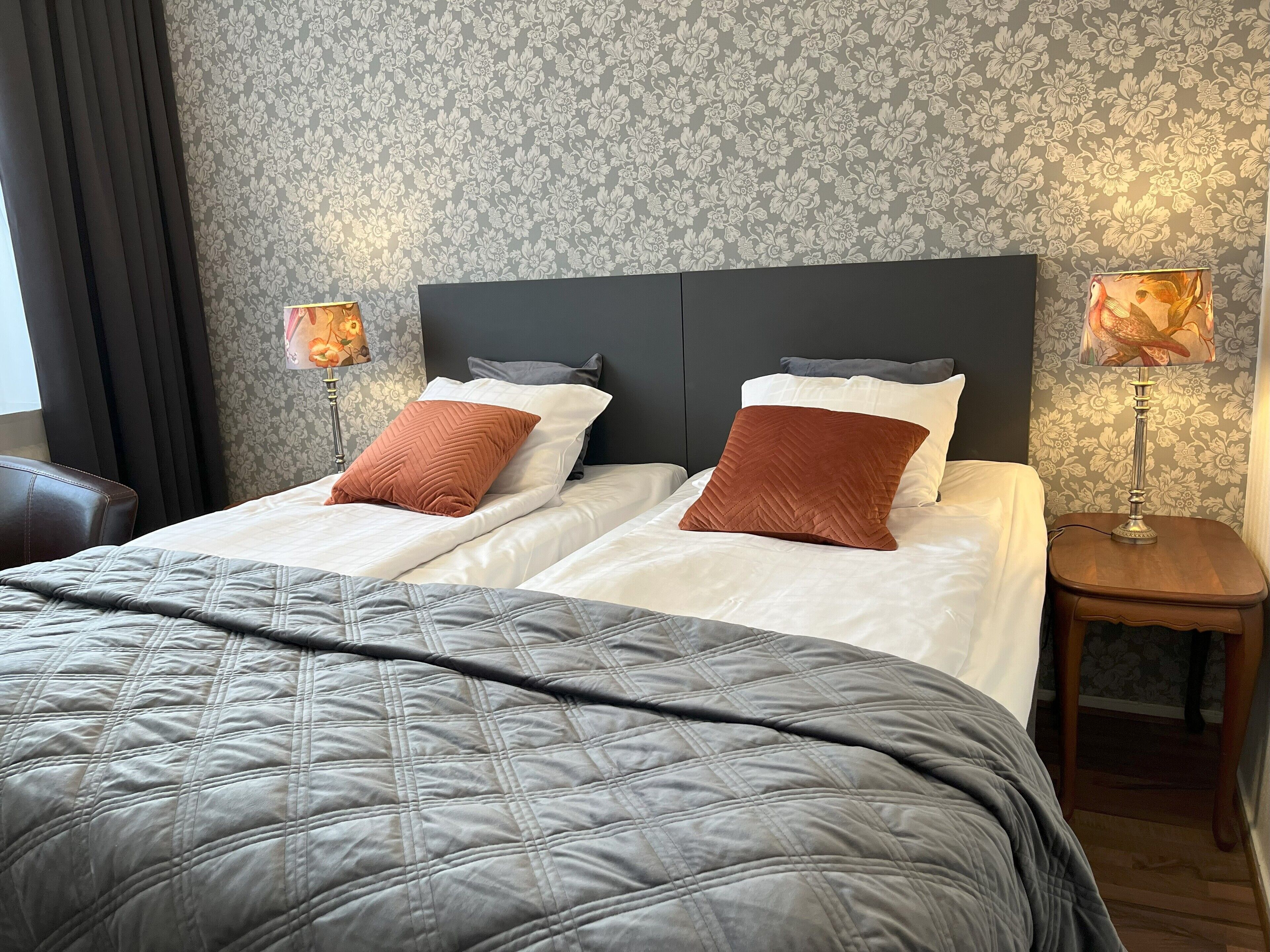 A hotel room with two beds, a large bedspread, a headboard, two nightstands with lamps, and a chair.