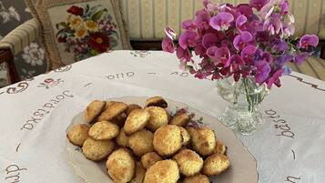 Um prato de biscoitos sobre uma mesa com toalha florida e um vaso de flores roxas.