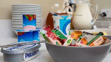 A kitchen counter with a bowl containing various packaged snacks, a container of Philadelphia ice cream, and stacks of white plates.