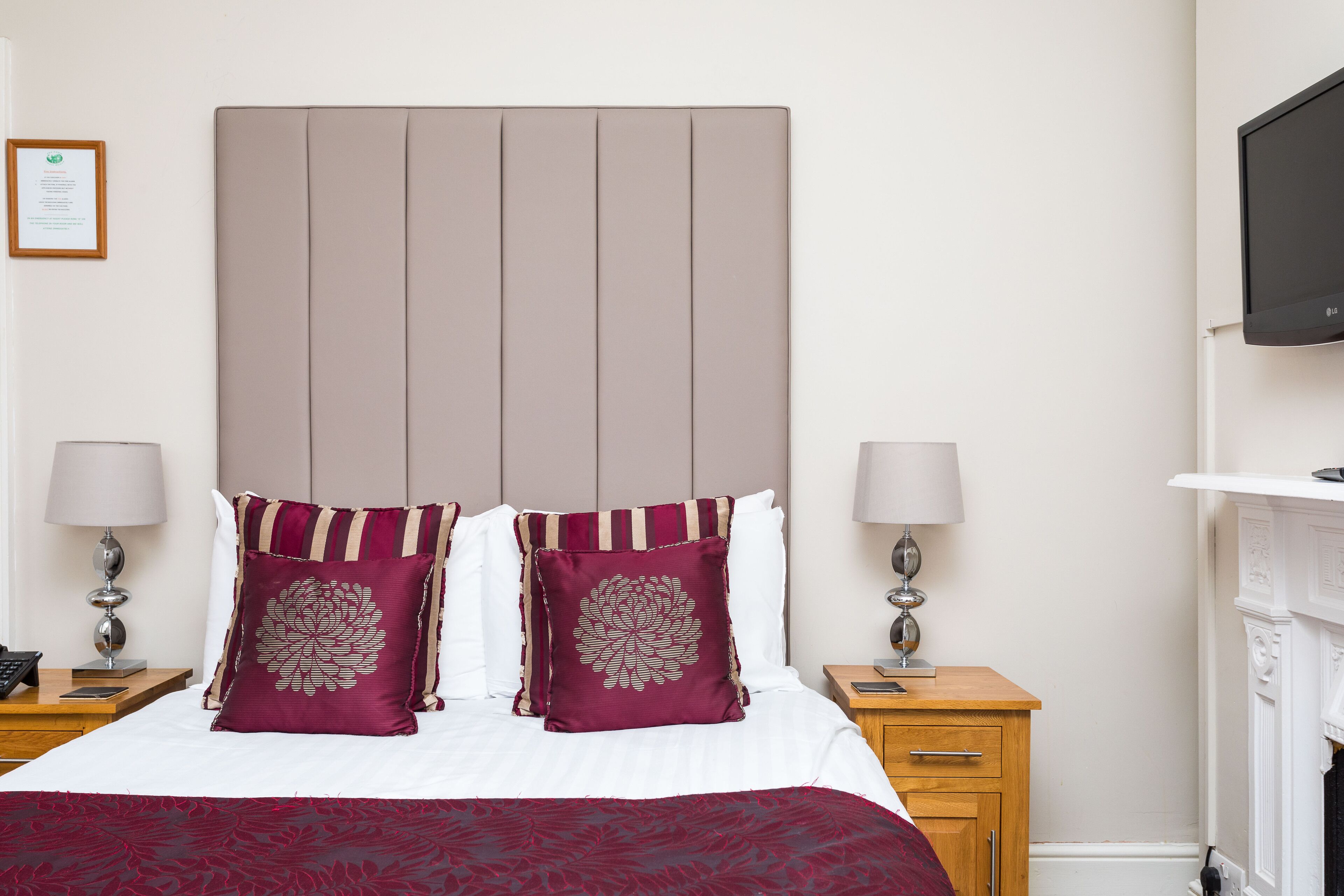 A neatly made bed with two decorative pillows, a bedside table with a lamp, and a television mounted on the wall.