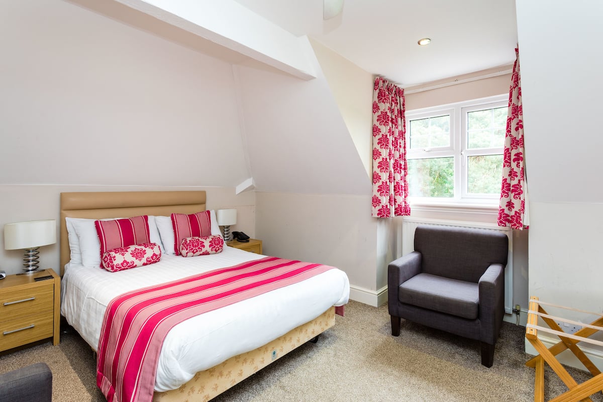 A bedroom with a bed, bedside table, lamp, chair, and window with curtains.
