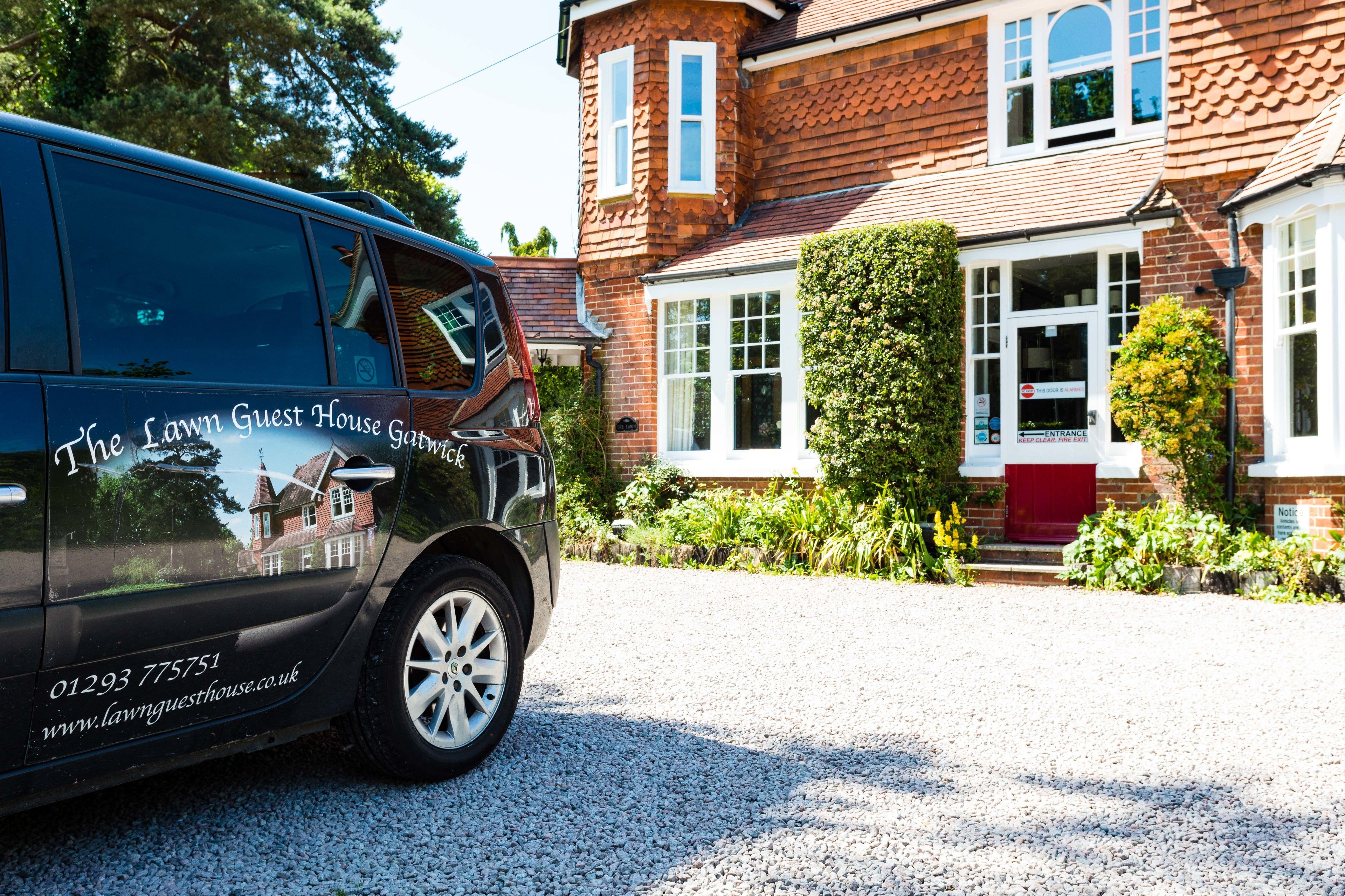 A black van parked in front of a red brick house with white windows and a red door.