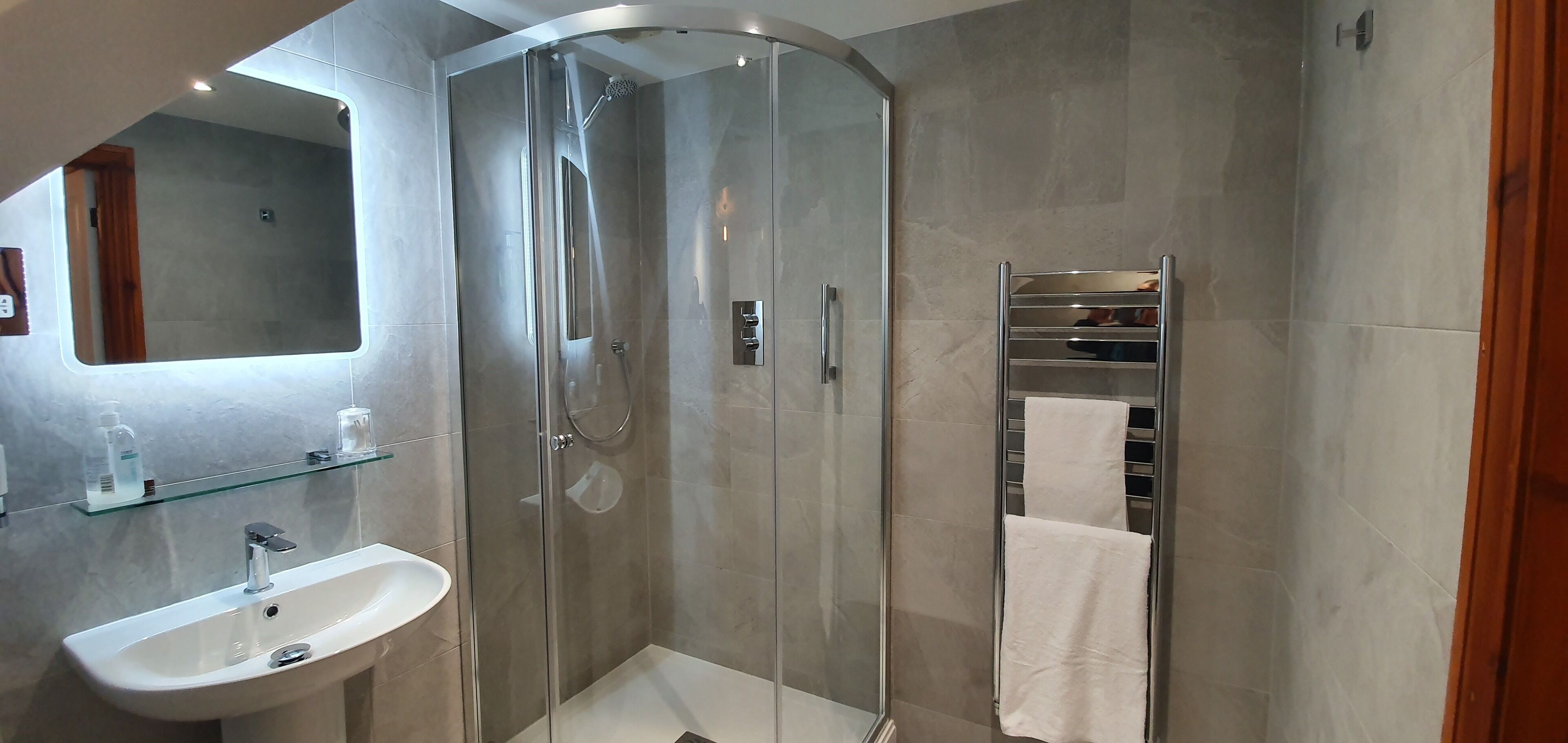 Ein modernes Badezimmer mit einer Duschkabine, einem weißen Waschbecken und einem Ablagefach aus Glas darüber.