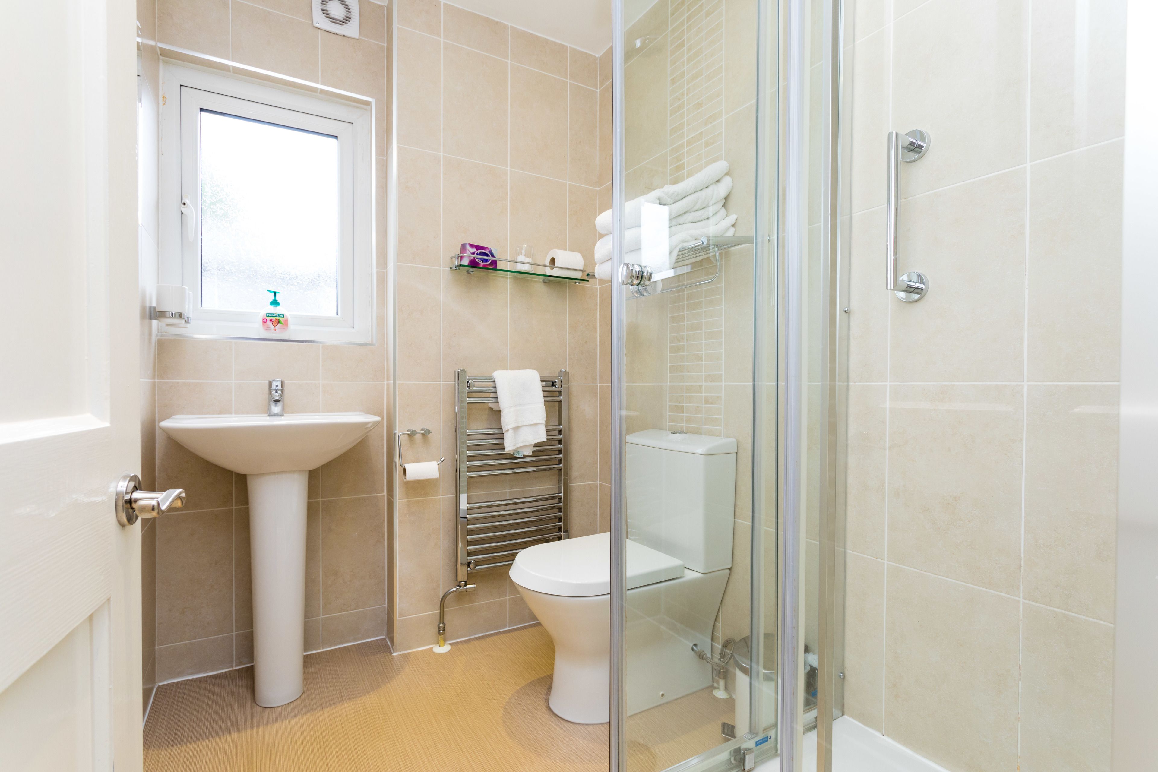 A bathroom with a pedestal sink, a toilet, a glass shower enclosure, and a towel rack.