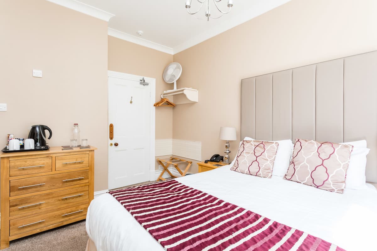 A hotel room with a bed, a wooden dresser, a desk with a lamp, and a mirror on the wall.