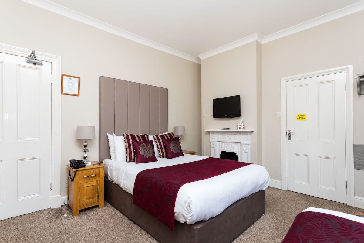 A hotel room with a bed, a nightstand, a television, and a fireplace.