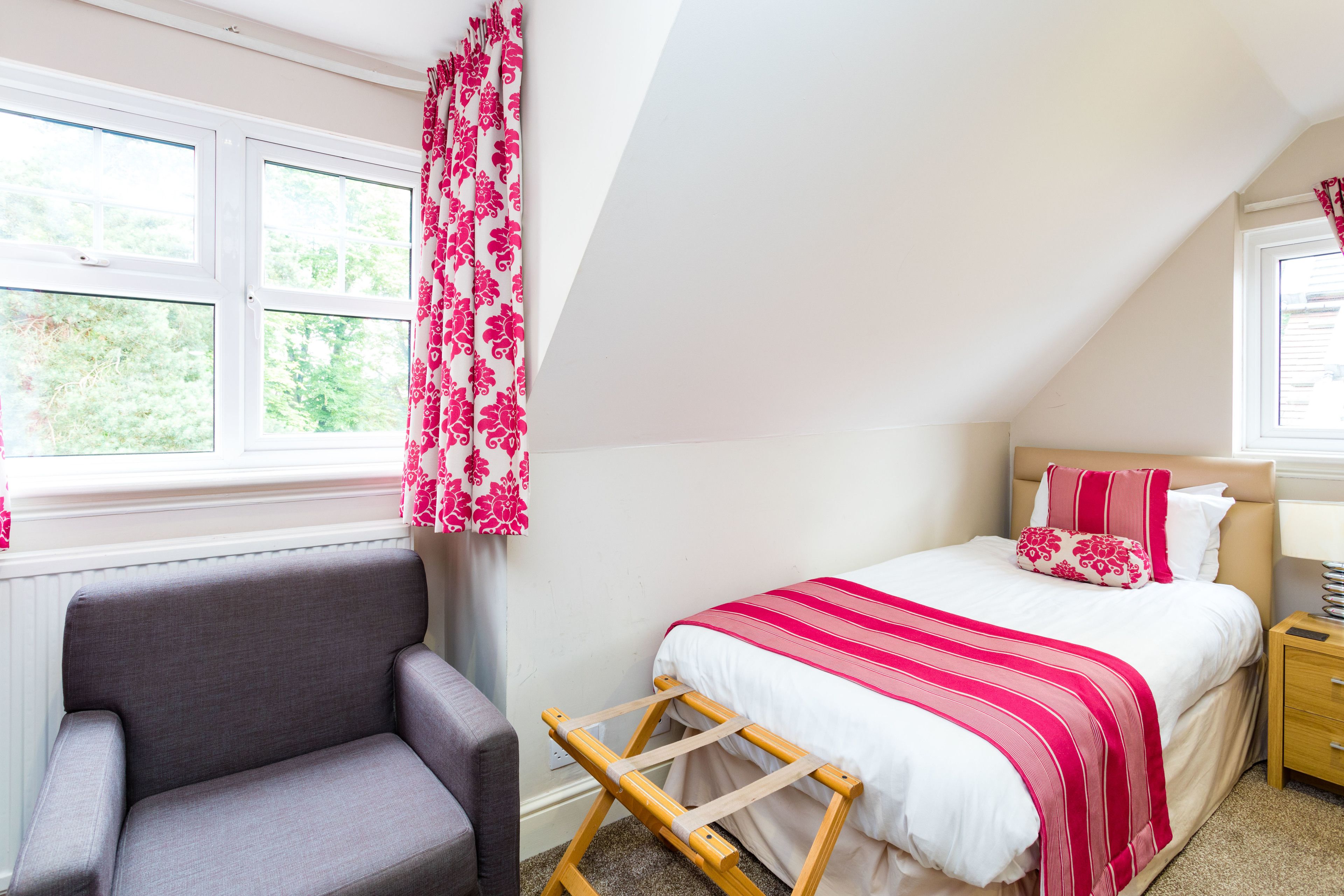 Une chambre à coucher avec un lit, une chaise, une échelle en bois et une fenêtre avec des rideaux.