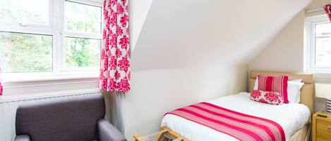 Une chambre à coucher avec un lit, une chaise, une échelle en bois et une fenêtre avec des rideaux.