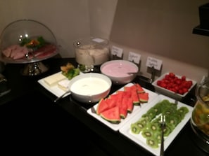 Een buffet met diverse gerechten, waaronder watermeloen, kiwi en een kom soep.