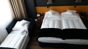 A hotel room with two beds, a wooden headboard, a small side table, and a window with curtains. - Hotel Lindenhof (Düsseldorf)