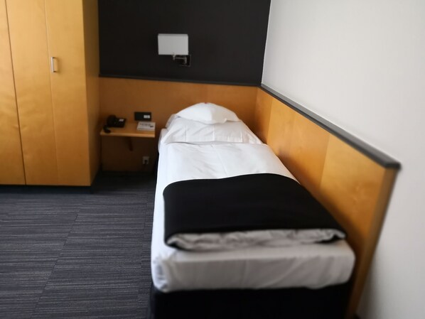 A single bed in a room with a wooden headboard, a small bedside table with a lamp, and a wall-mounted light fixture. - Hotel Lindenhof (Düsseldorf)