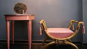 A room with a dark grey wall, a wooden side table with a vase, and a golden chair with tassels. - Hotel Lindenhof (Düsseldorf)