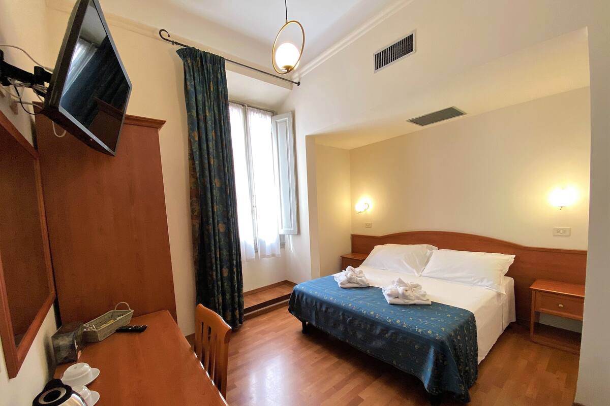 Une chambre d’hôtel avec un lit, un bureau, une télévision et une fenêtre avec des rideaux.