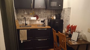 Eine kleine Küche mit dunklen Schränken, einer Mikrowelle, einer Kaffeemaschine und einem Essbereich mit Tisch und Stühlen.