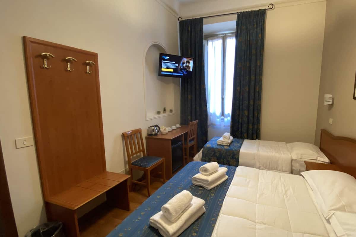 Une chambre d’hôtel avec deux lits, un bureau, une chaise, une télévision et une armoire.