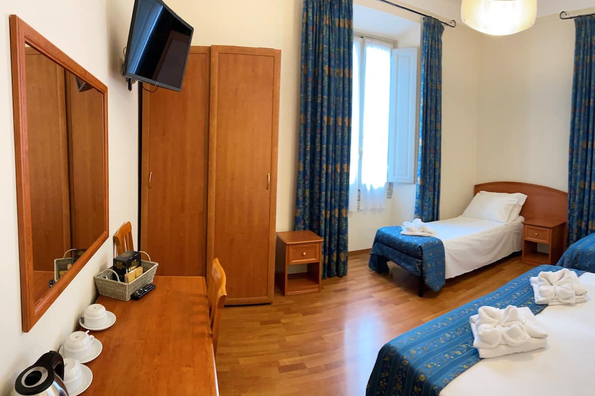 Une chambre d’hôtel avec deux lits, une armoire en bois, une télévision et une petite table avec un panier et des tasses.