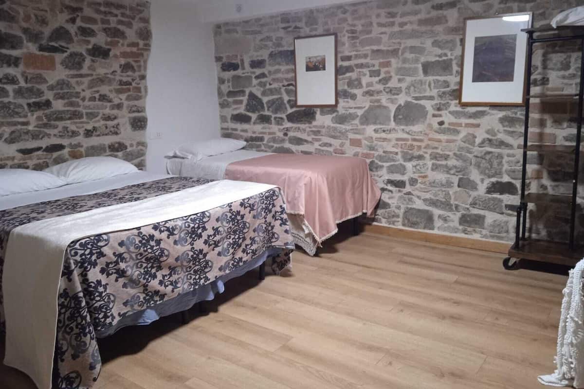 Une chambre avec deux lits, un mur en pierre et un plancher en bois.
