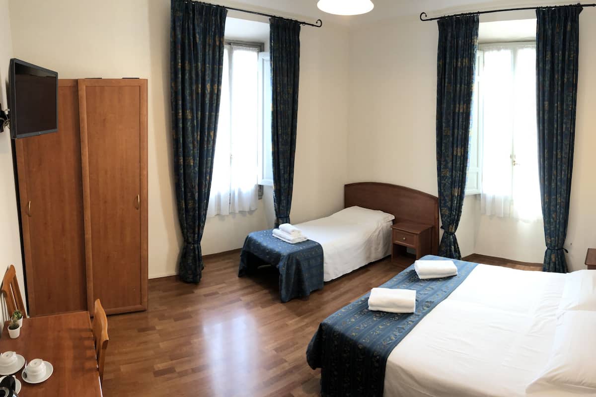 Une chambre d’hôtel avec deux lits simples, une armoire en bois, une petite table avec une chaise et un téléviseur fixé au mur.