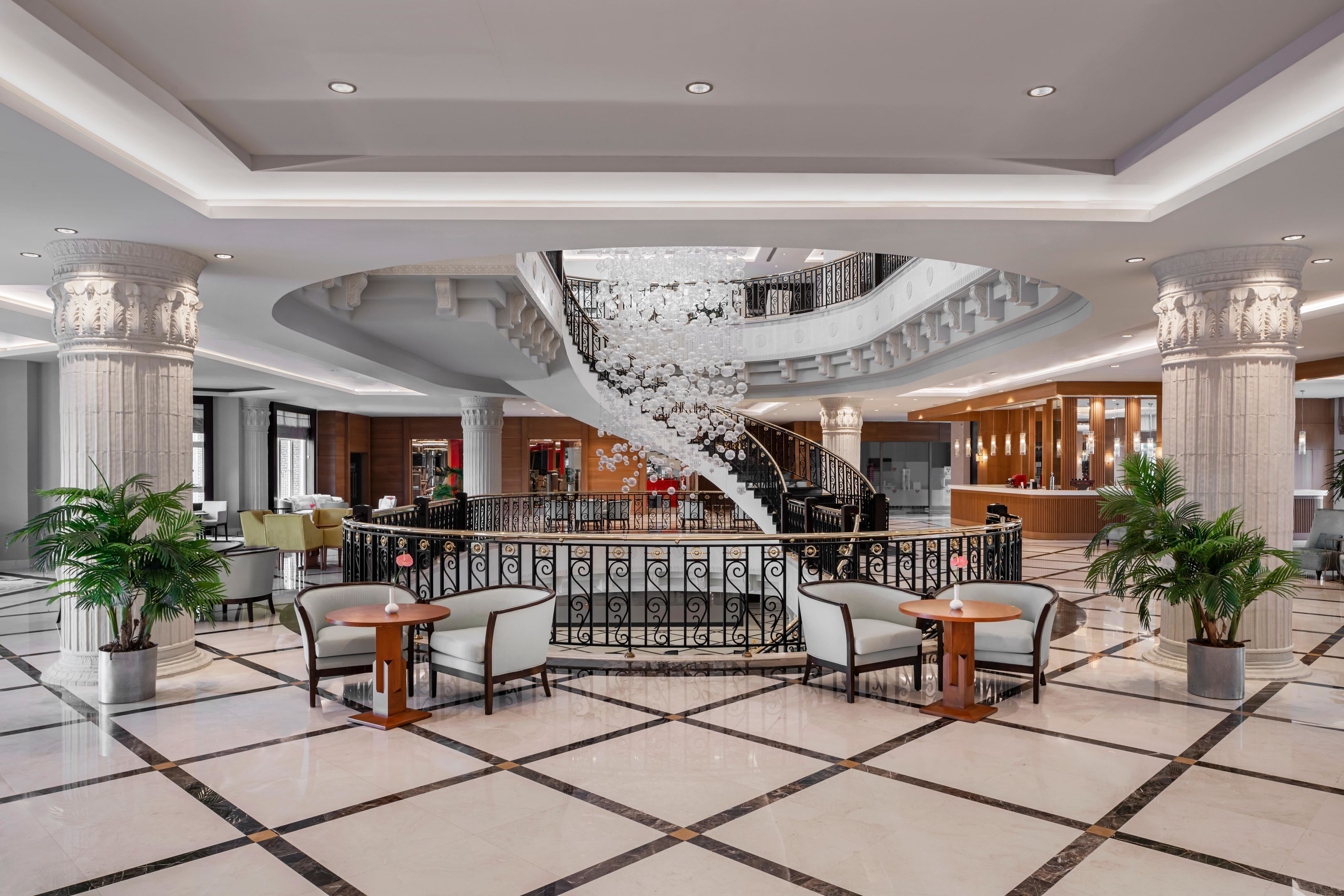A spacious lobby with a central spiral staircase, marble flooring, and seating areas.