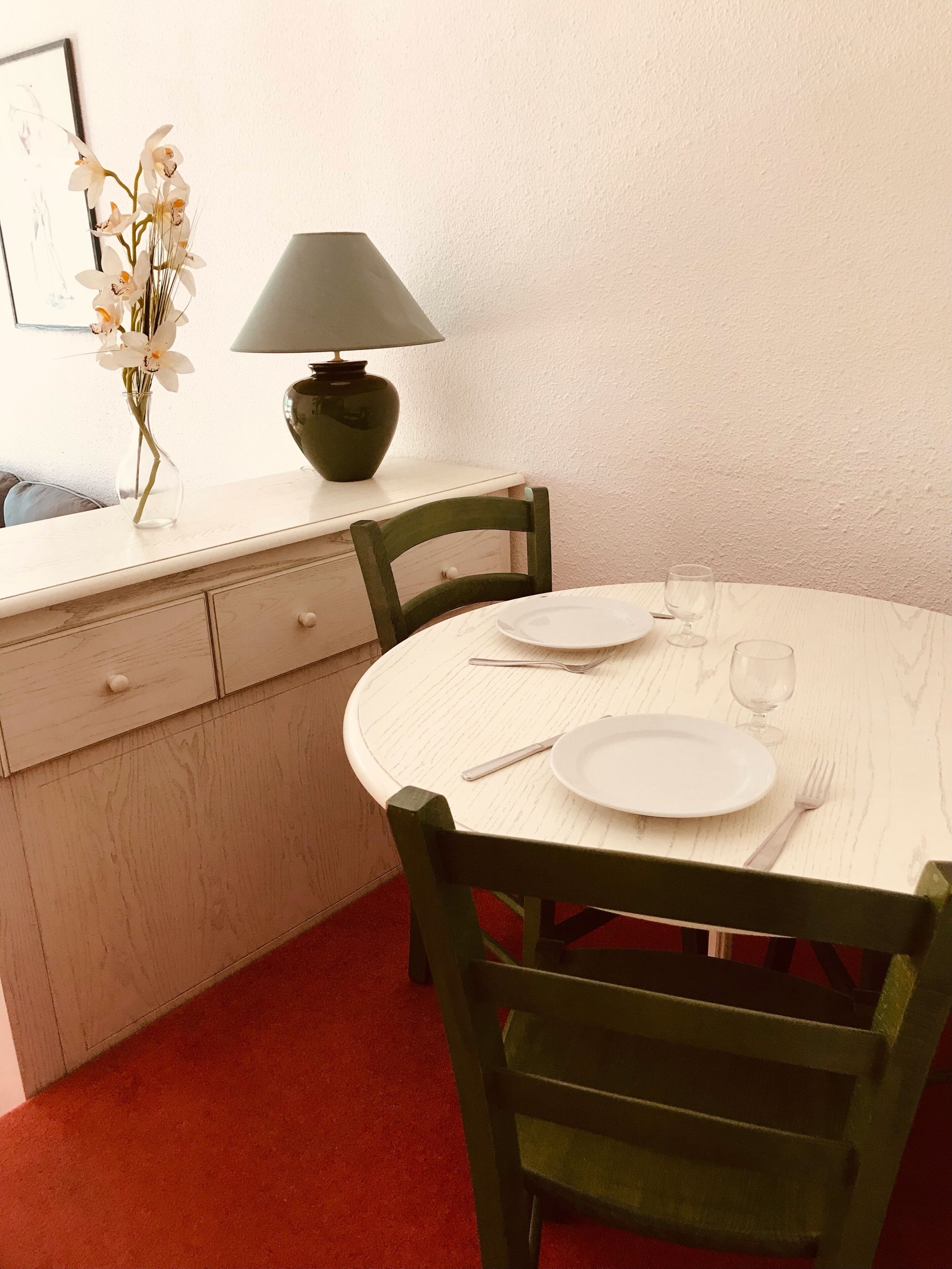 Een eetgedeelte met een ronde tafel, stoelen, een lamp en een vaas met bloemen.