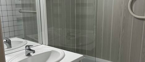 A bathroom with a white sink, a mirror, and a glass shower enclosure.