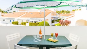 A table with a green umbrella, wine glasses, a bottle, and a fruit platter. - Résidence Lagrange Vacances Les Fermettes de la Mer (Saint-Jean-de-Monts)