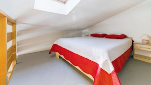 A bedroom with a skylight, a bed with red and white bedding, a wooden nightstand, and a bedside table with a lamp. - Résidence Lagrange Vacances Les Fermettes de la Mer (Saint-Jean-de-Monts)