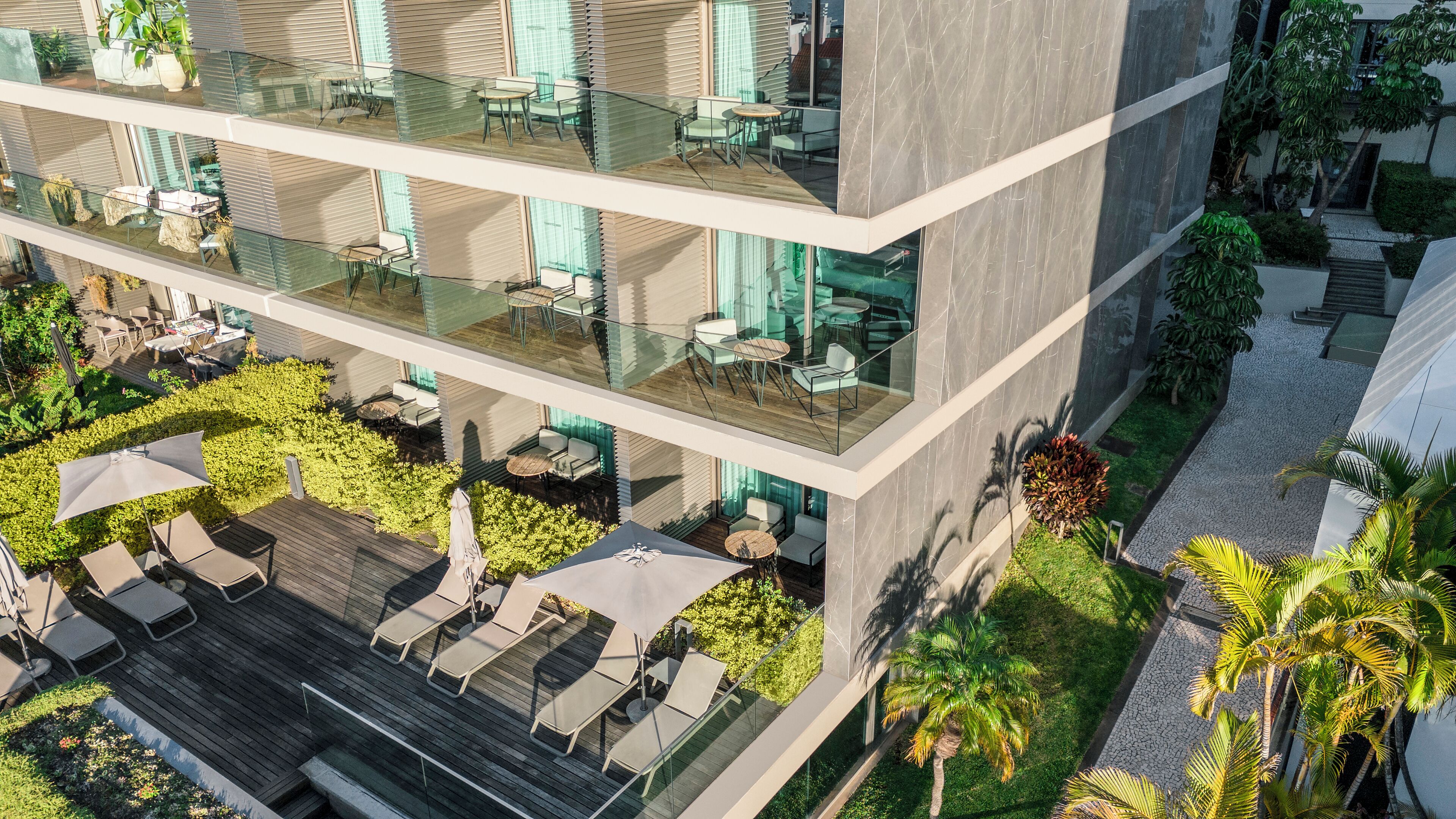 A multi-story building with outdoor seating areas, glass railings, and a landscaped garden.
