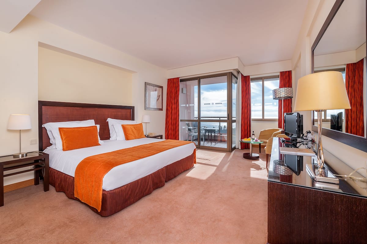 Une chambre d’hôtel avec un grand lit, un bureau avec un ordinateur, une télévision et une vue sur la ville par la fenêtre.