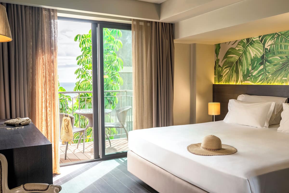 Une chambre d’hôtel équipée d’un lit, d’un bureau, d’une chaise et d’un balcon donnant sur un espace verdoyant.