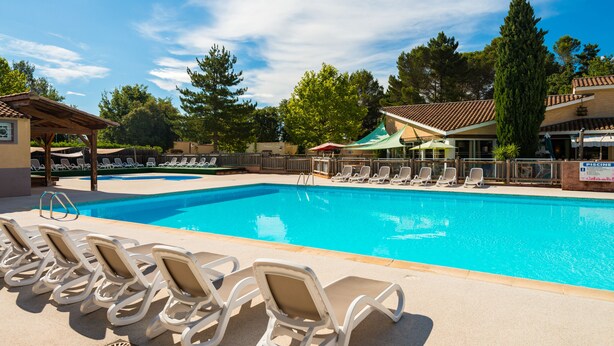 A swimming pool with lounge chairs, a covered seating area, and a sign for a 'PISCINE'.