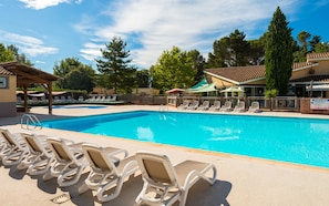 A swimming pool with lounge chairs, a covered seating area, and a sign for a 'PISCINE'.