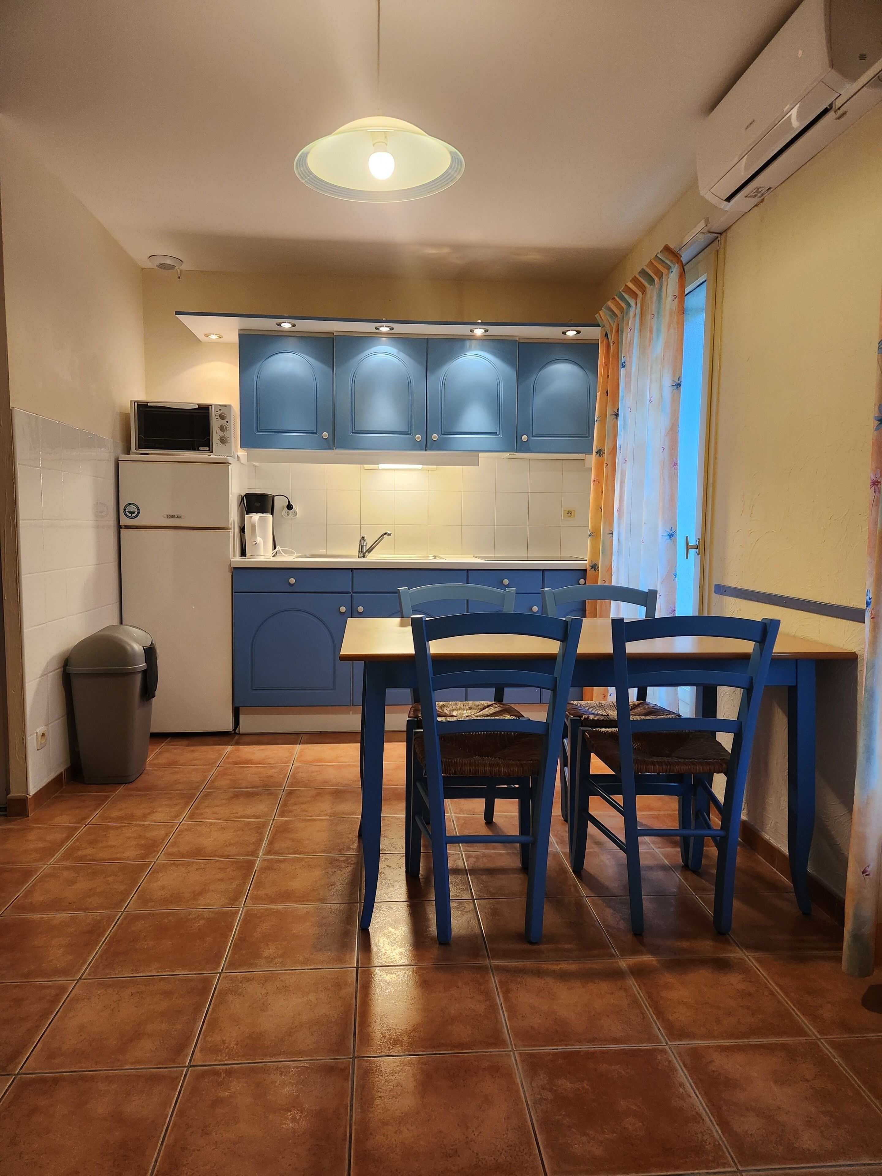 A compact kitchen with blue cabinets, a microwave, a sink, and a dining table with chairs.