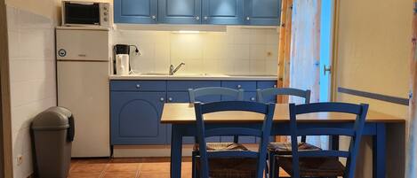 A compact kitchen with blue cabinets, a microwave, a sink, and a dining table with chairs.