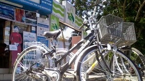 A bicycle with a basket parked in front of a building with various signs and advertisements. - Stars Hotel 26 Bat Su (Hanoi)