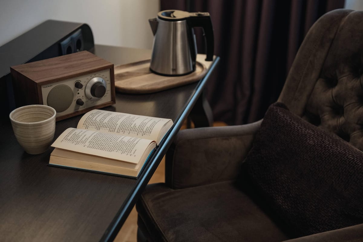 A wooden table with a radio, a kettle, a book, and a cup.