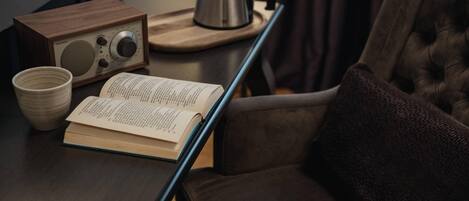 A wooden table with a radio, a kettle, a book, and a cup.