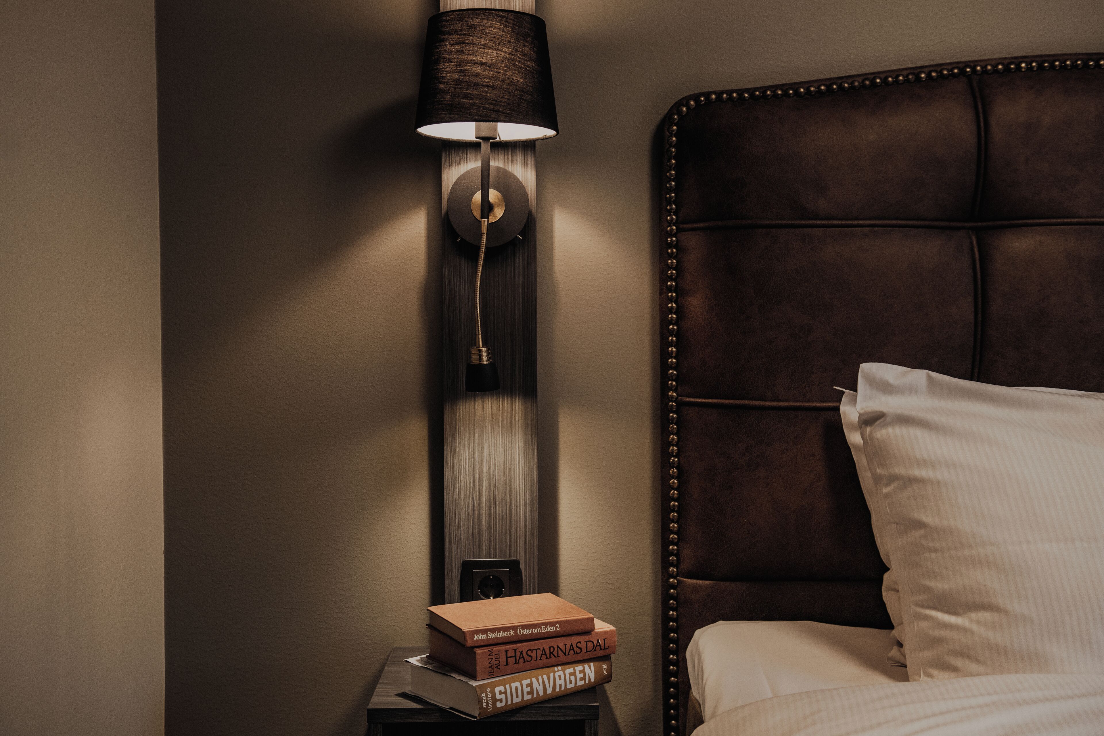 A bedside table with books and a wall-mounted lamp.