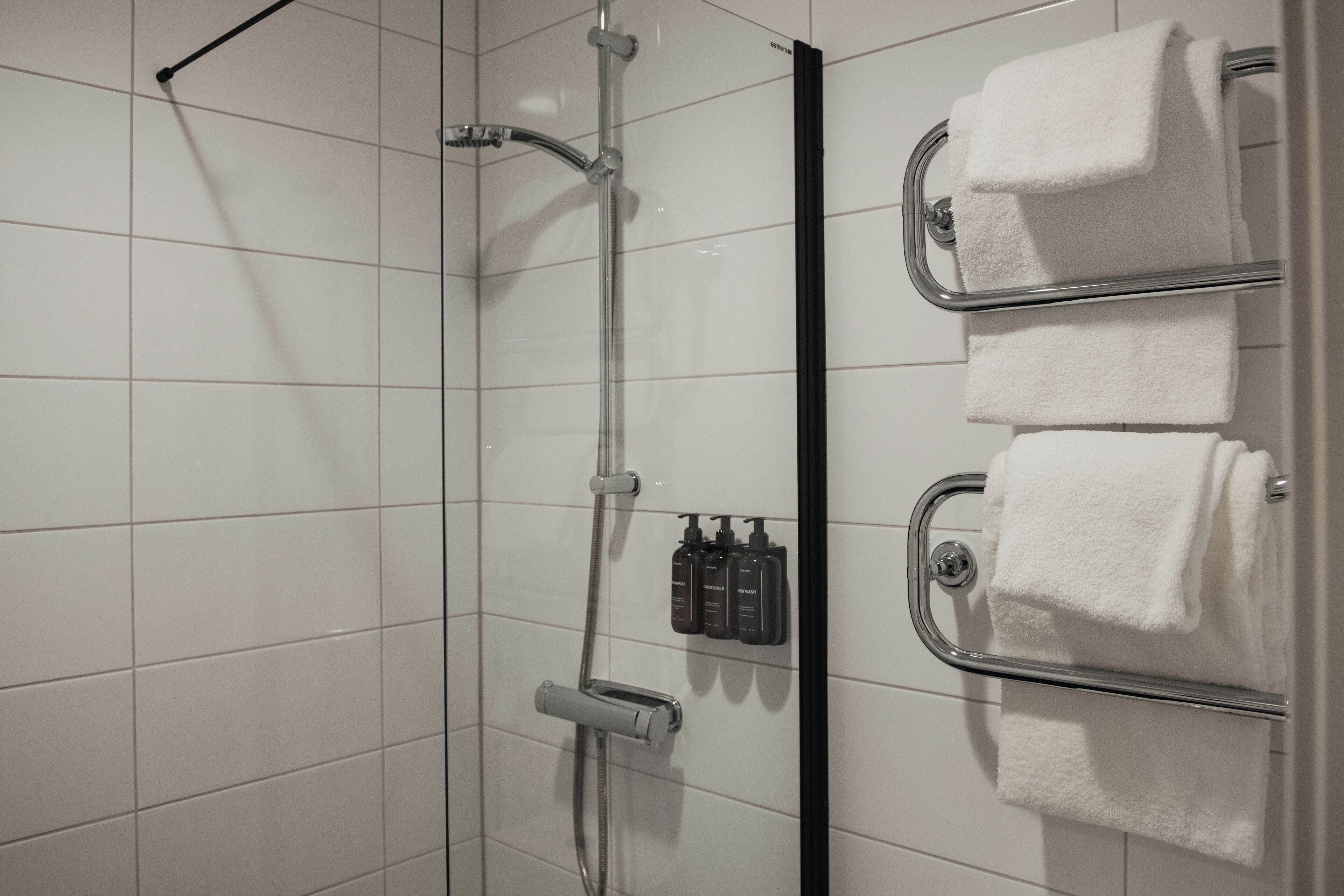 A shower with a glass door, a towel rack with three towels, and a set of toiletries.