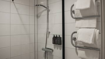A shower with a glass door, a towel rack with three towels, and a set of toiletries.