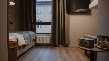 A hotel room with a bed, a table with a radio, a TV, and a window with curtains.