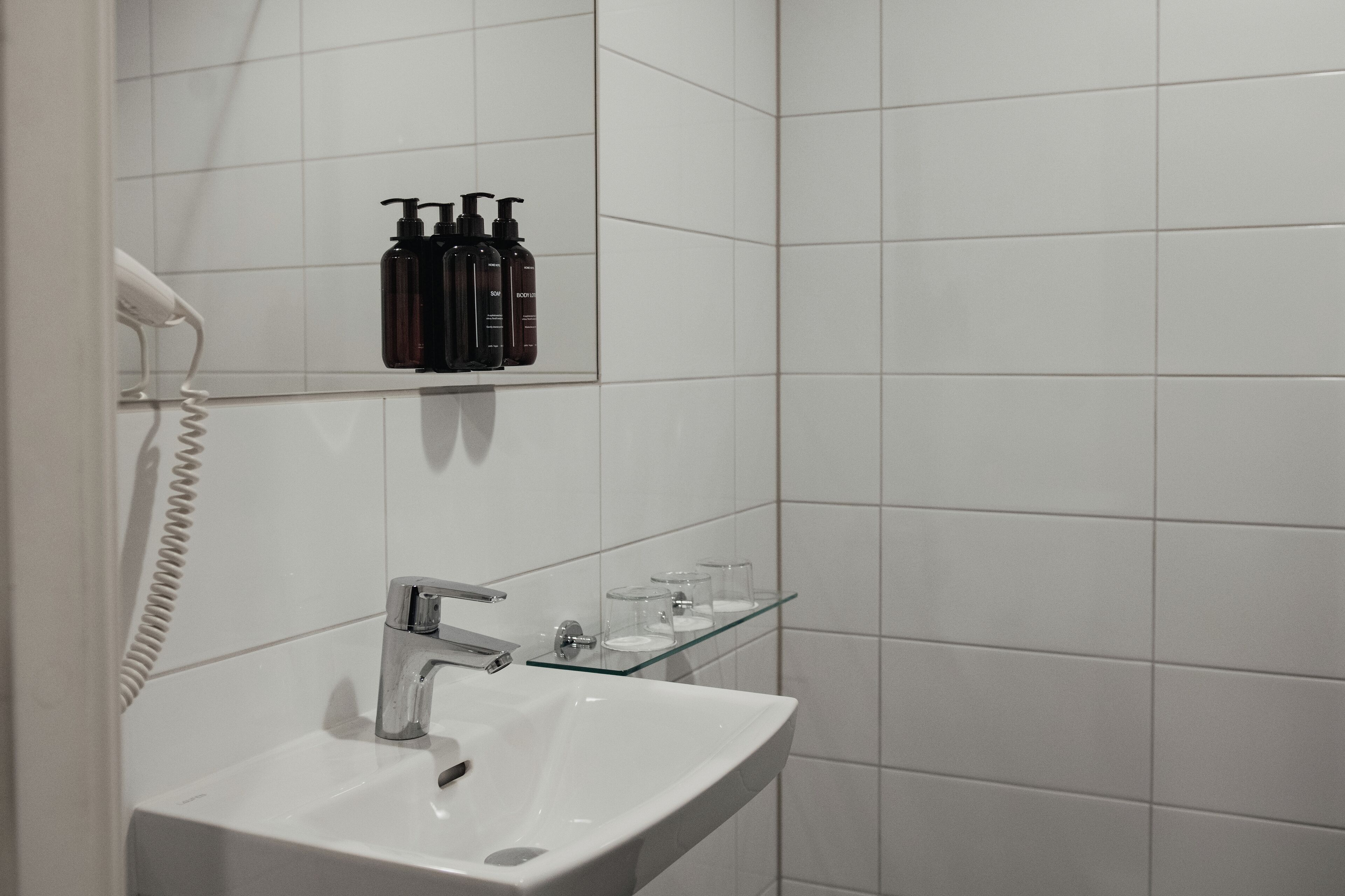 A bathroom with a white sink, a mirror, a telephone, and toiletries on a shelf.