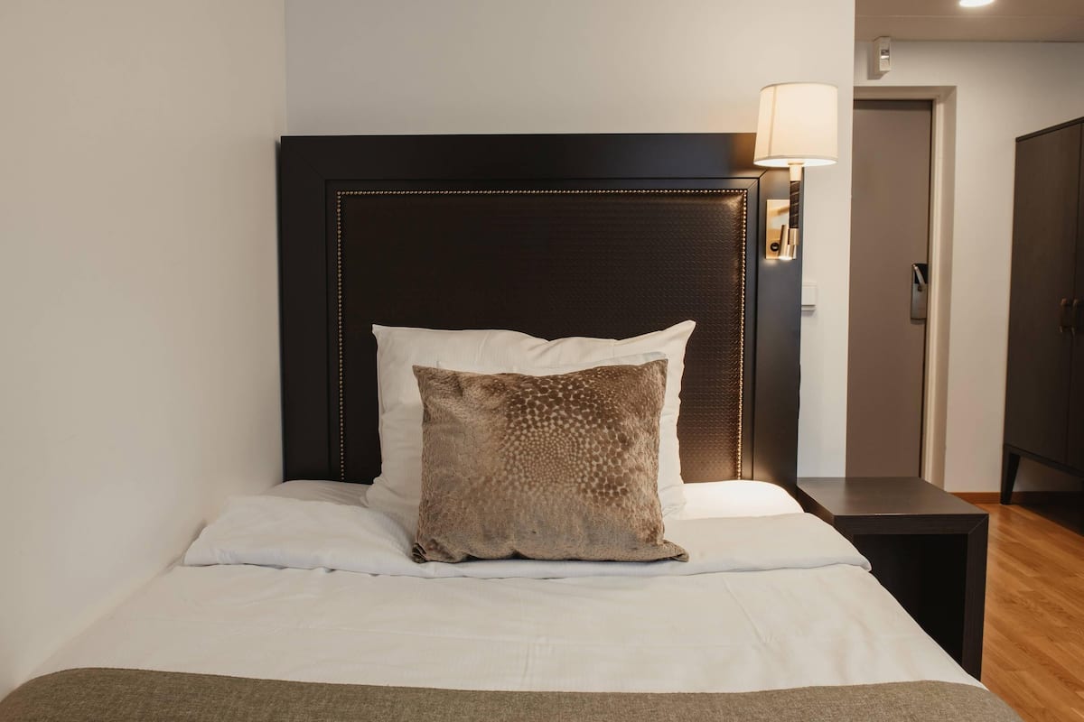 A hotel room with a bed, a nightstand, a lamp, and a wardrobe.