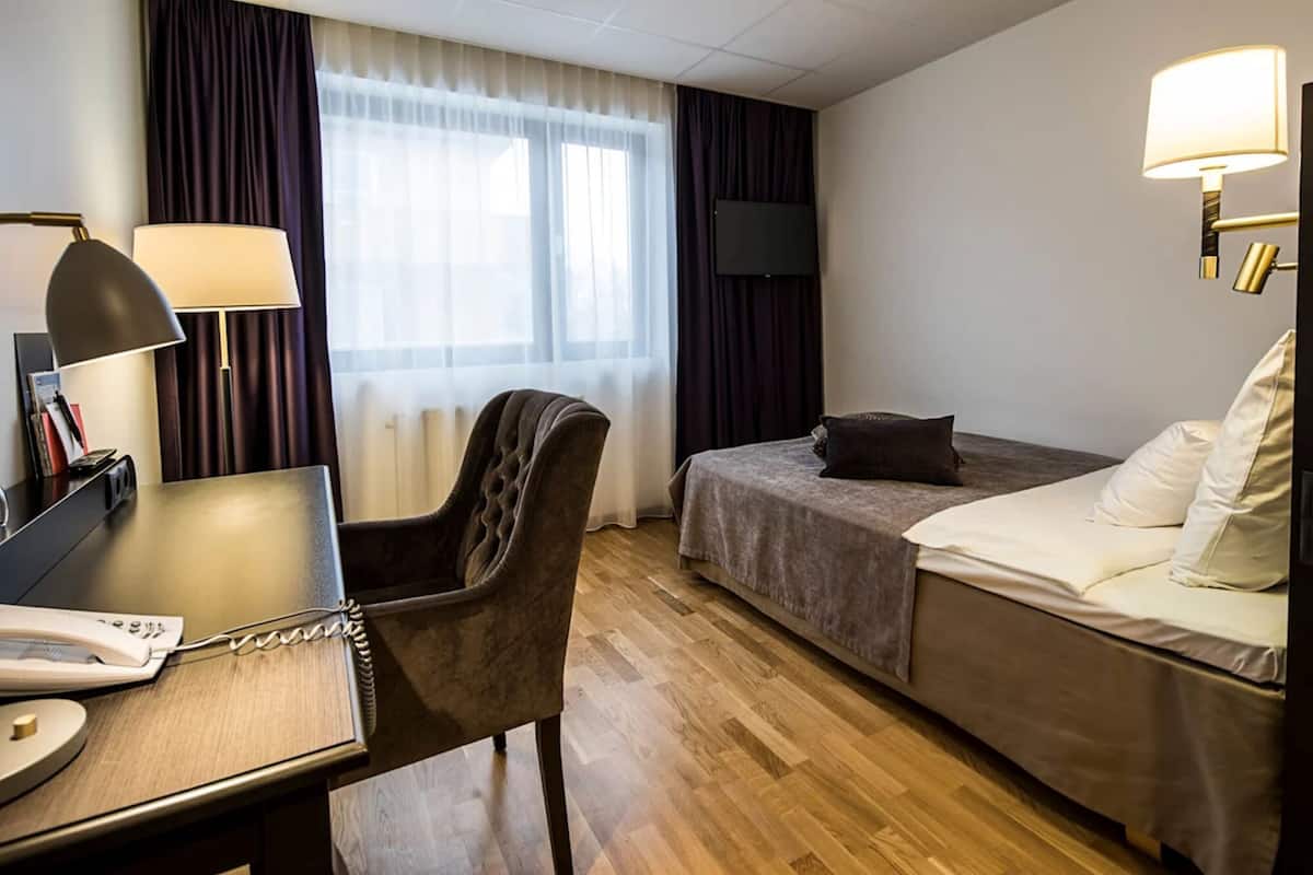 A hotel room with a desk, chair, bed, and a television.