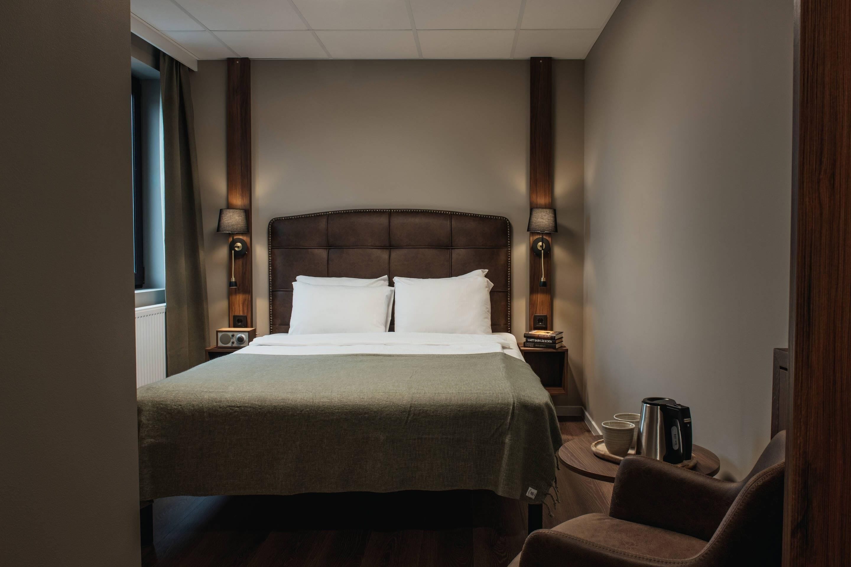 Une chambre d’hôtel comprenant un lit, deux lampes de chevet, une chaise, une machine à café et une petite table.