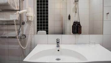 A bathroom with a white sink, a towel rack with towels, a hairdryer, and a shower with a handheld showerhead.