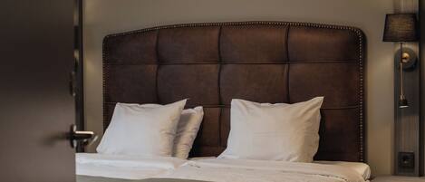 Una habitación de hotel con una cama grande, una mesita de noche, una lámpara y una puerta.