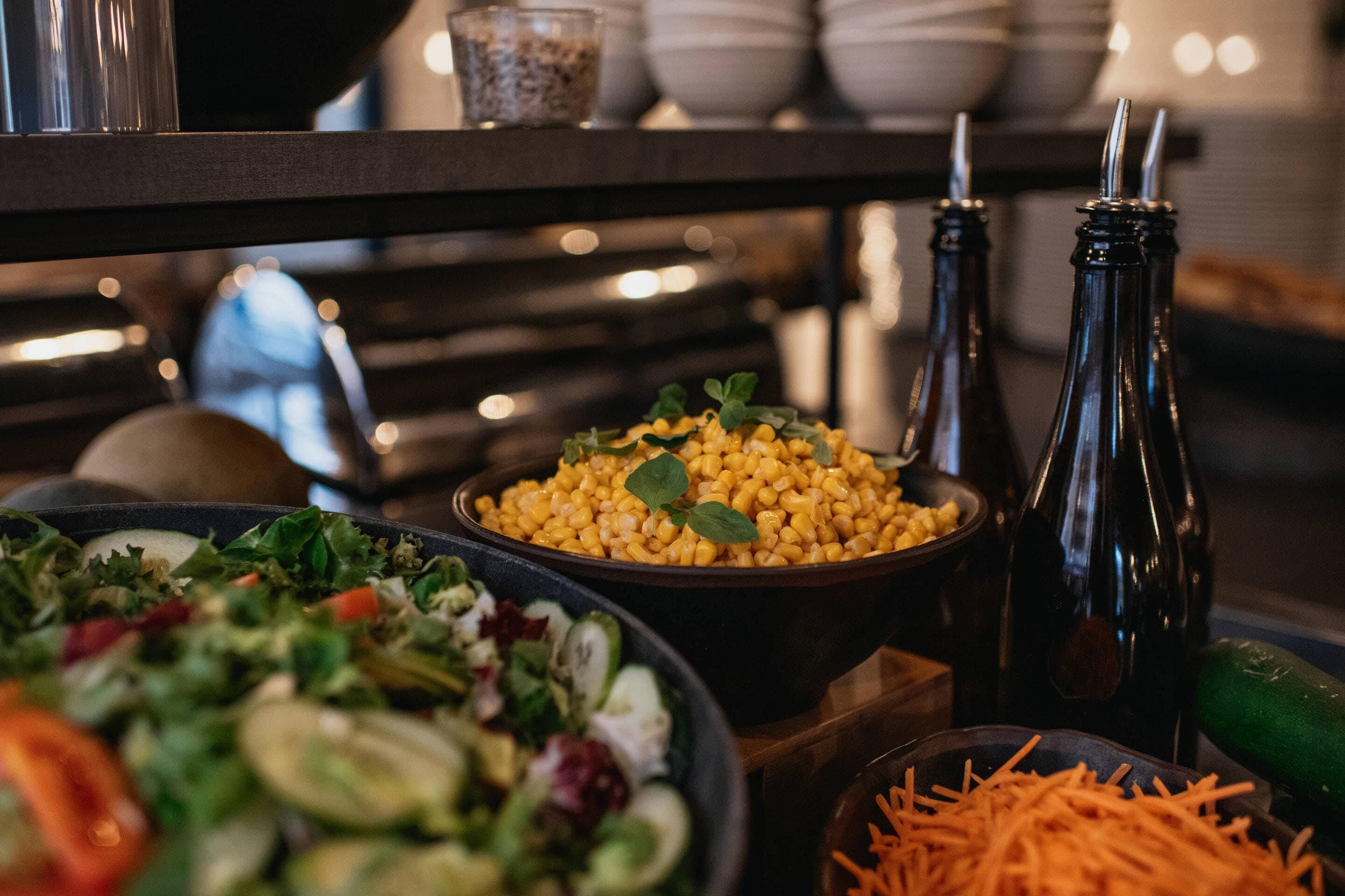 A buffet table with various dishes, including a salad, corn, and shredded carrots.