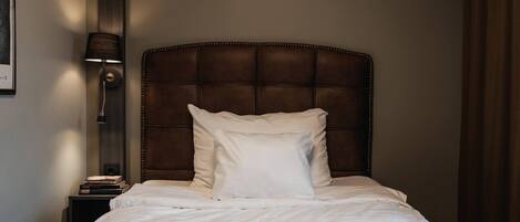 A neatly made bed with a headboard, a bedside lamp, and a stack of books on a nightstand.